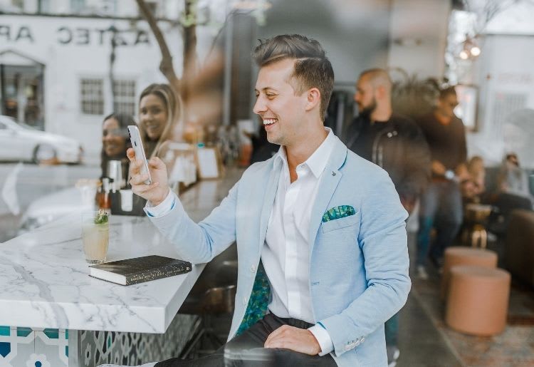 A young man smiles at his phone in a busy cafe